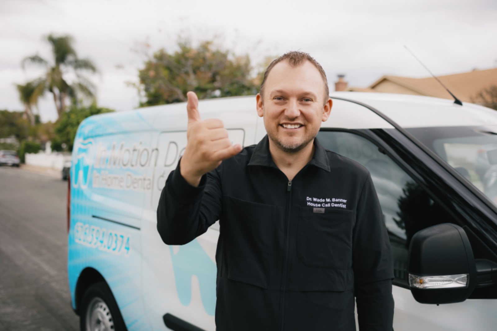 Male dentist in black jacket standing by mobile dental van at residential home