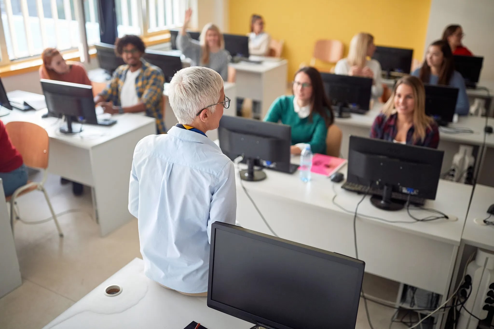 An instructor in a computer lab lectures to a group of adult learners