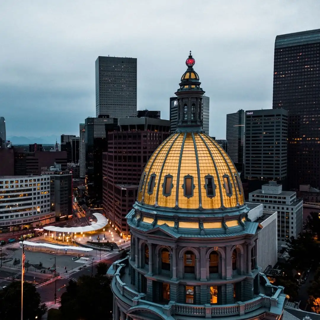 Colorado State Capitol dome illuminated at dusk with Denver skyline in background