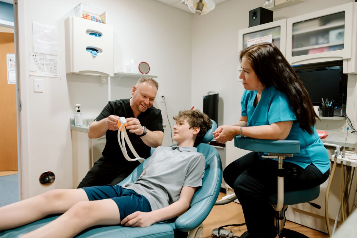Pediatric dentist examining a child patient in dental chair with staff member present