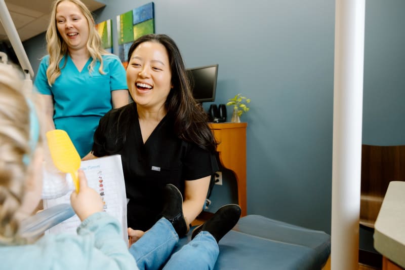 Female dental provider in teal scrubs smiling with young patient in treatment room