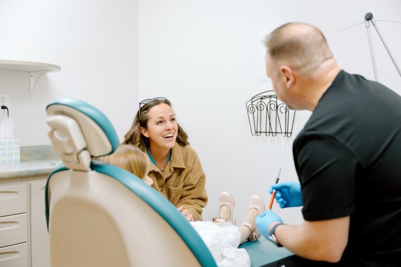 Dentist in gloves preparing or discussing dental procedure with patient in chair