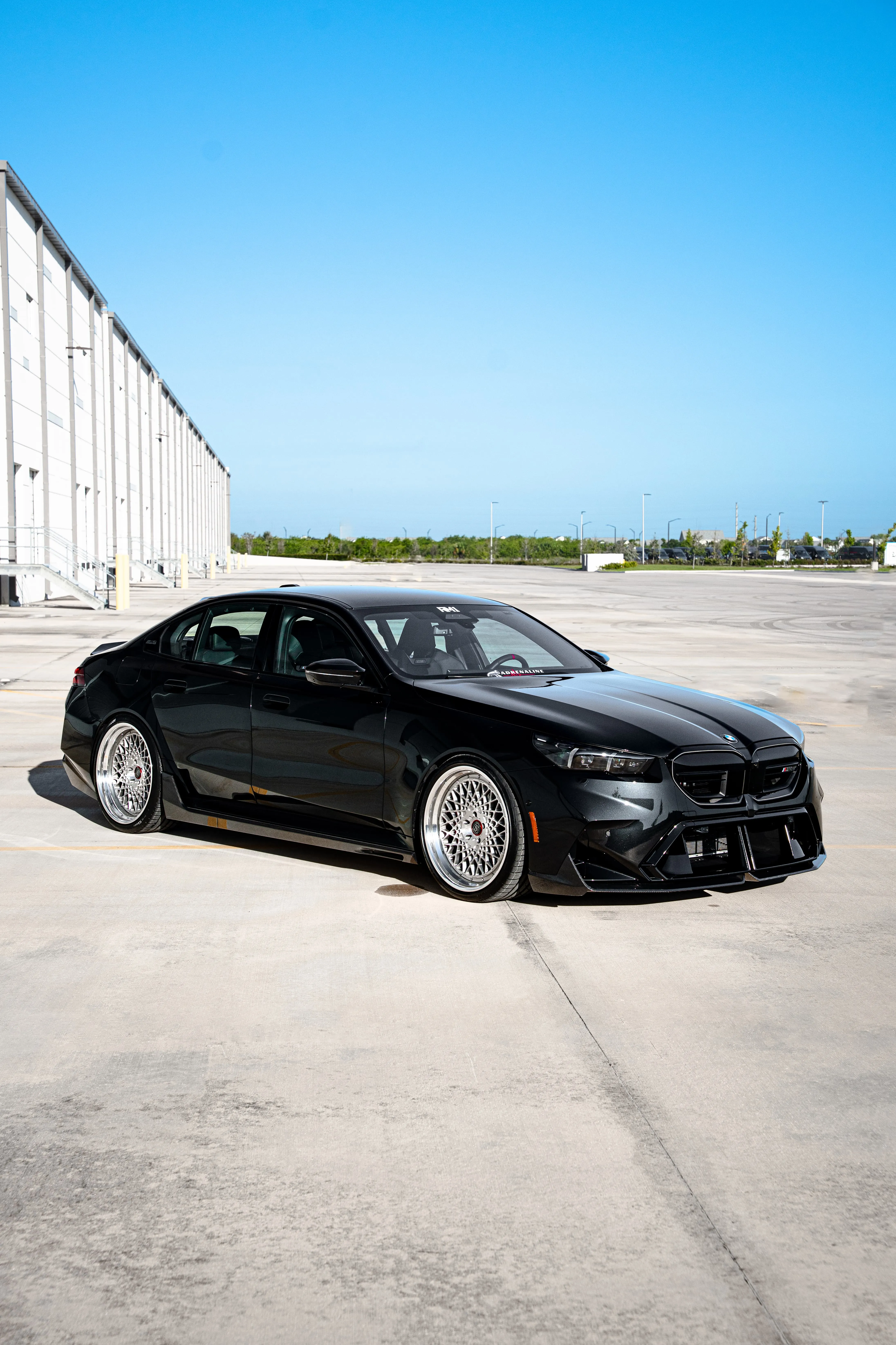 Black lowered BMW sedan with aftermarket wheels parked in industrial lot