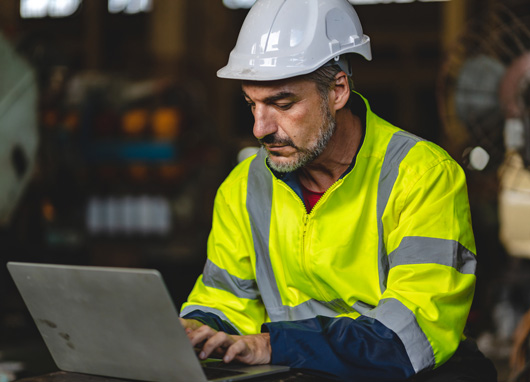 stock photo man in safety vest and hard hat using laptop