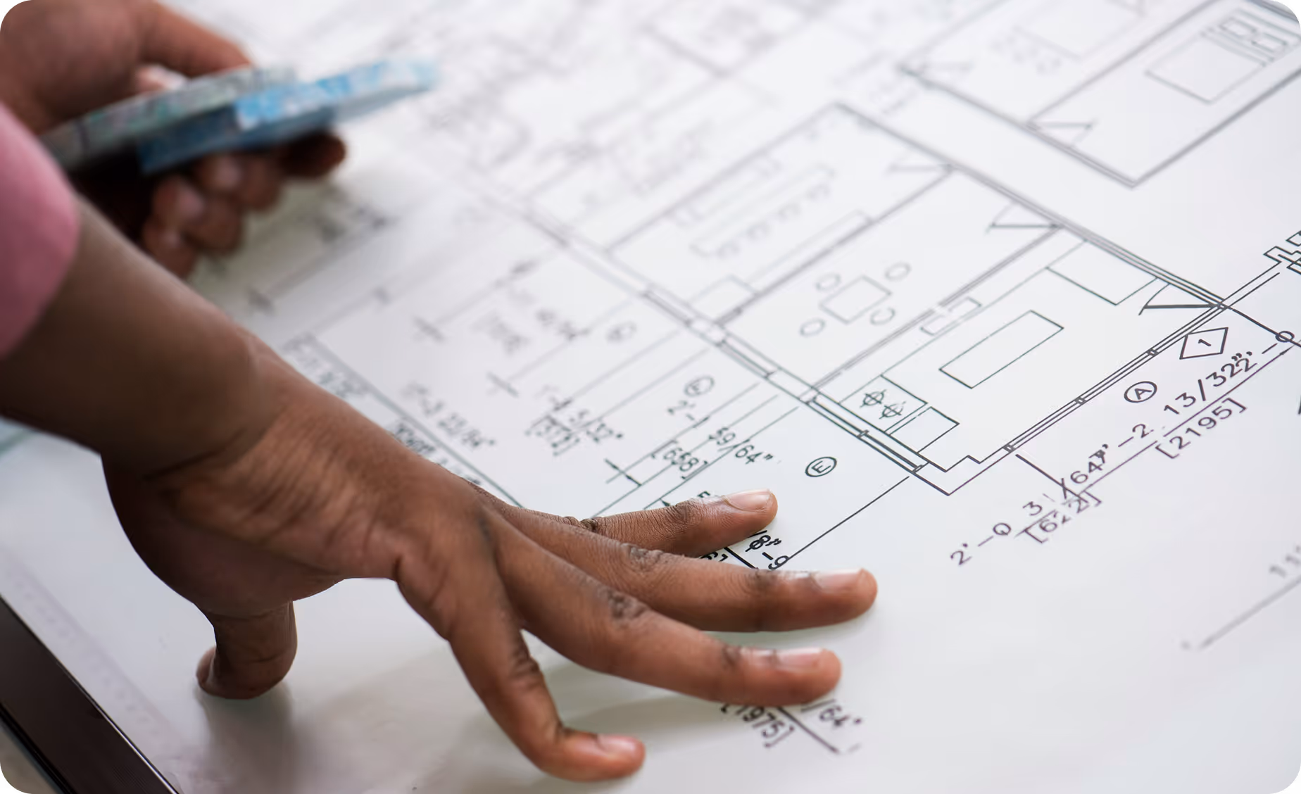 a picture of building plans, spread out on a desk, with a person's hands holding them in place.