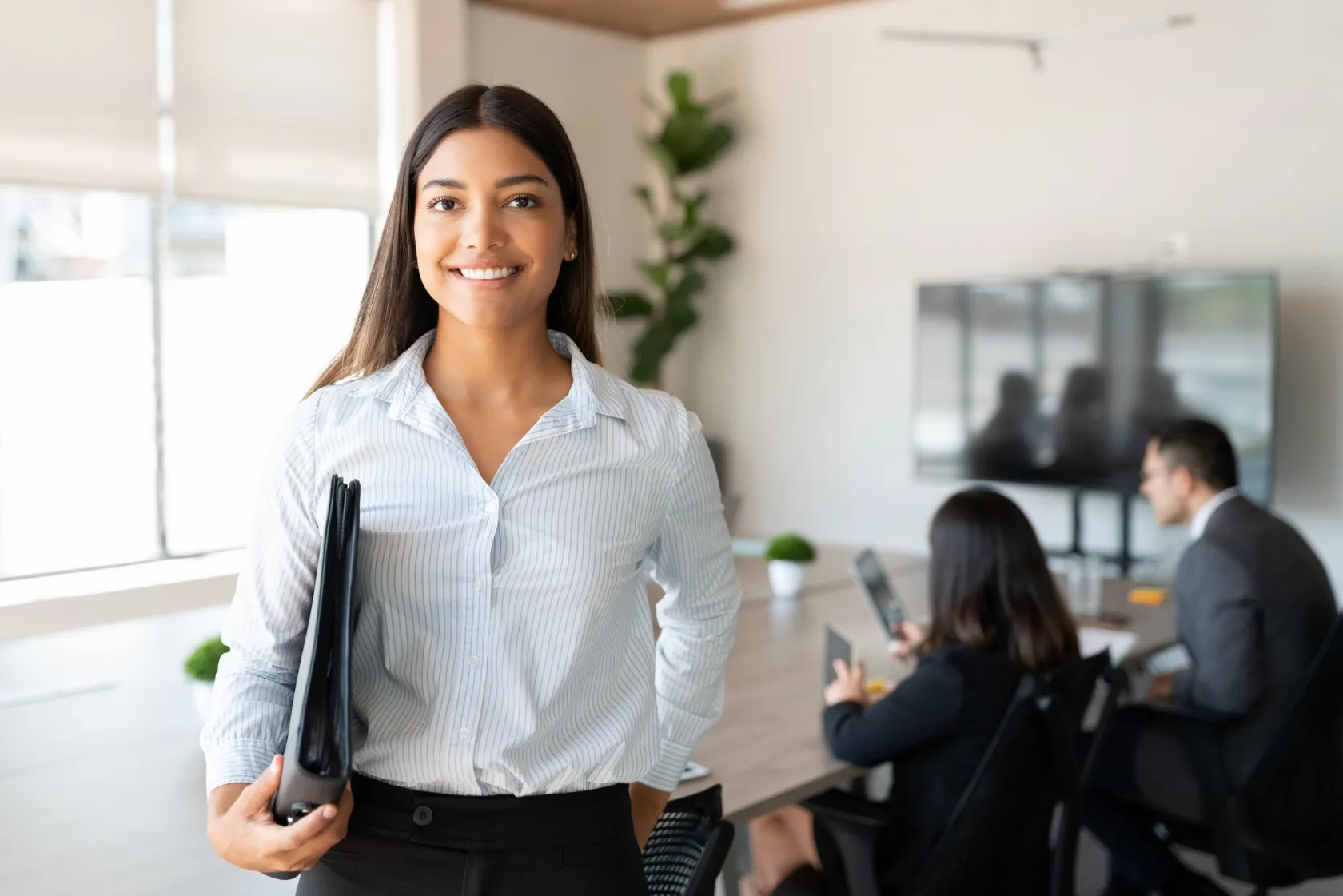 A smiling businesswoman standing in front of a team in a conference room