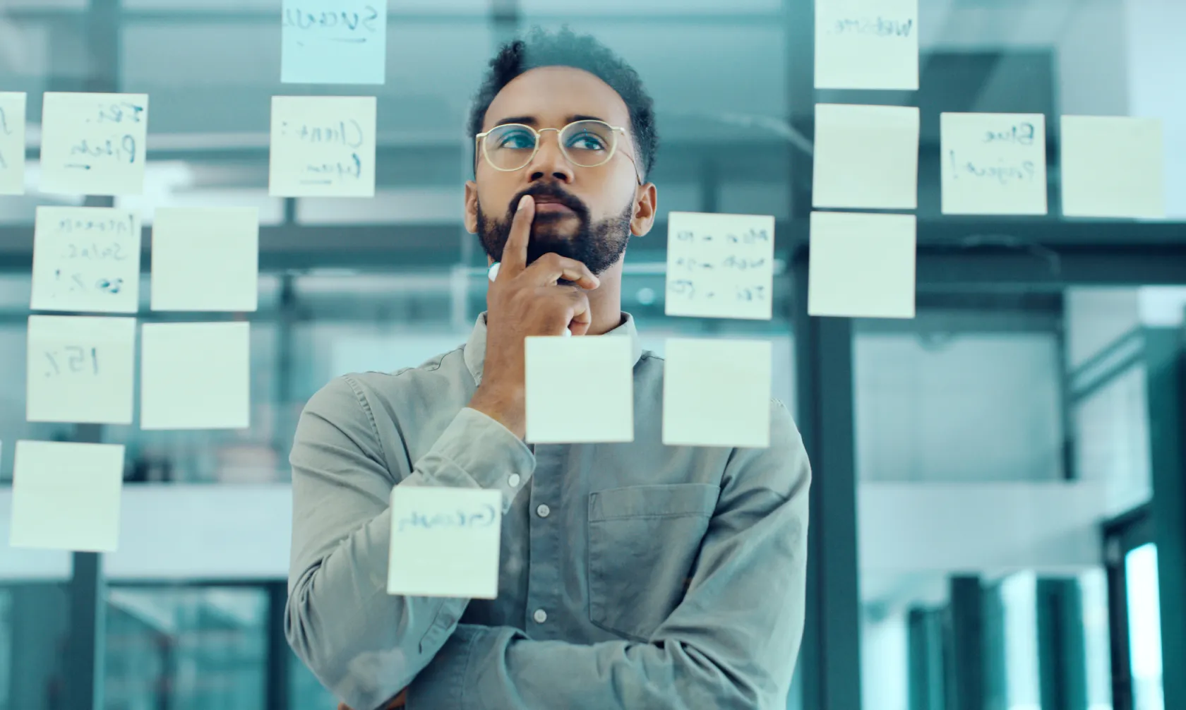 A man deliberating while looking at post it notes on a wall