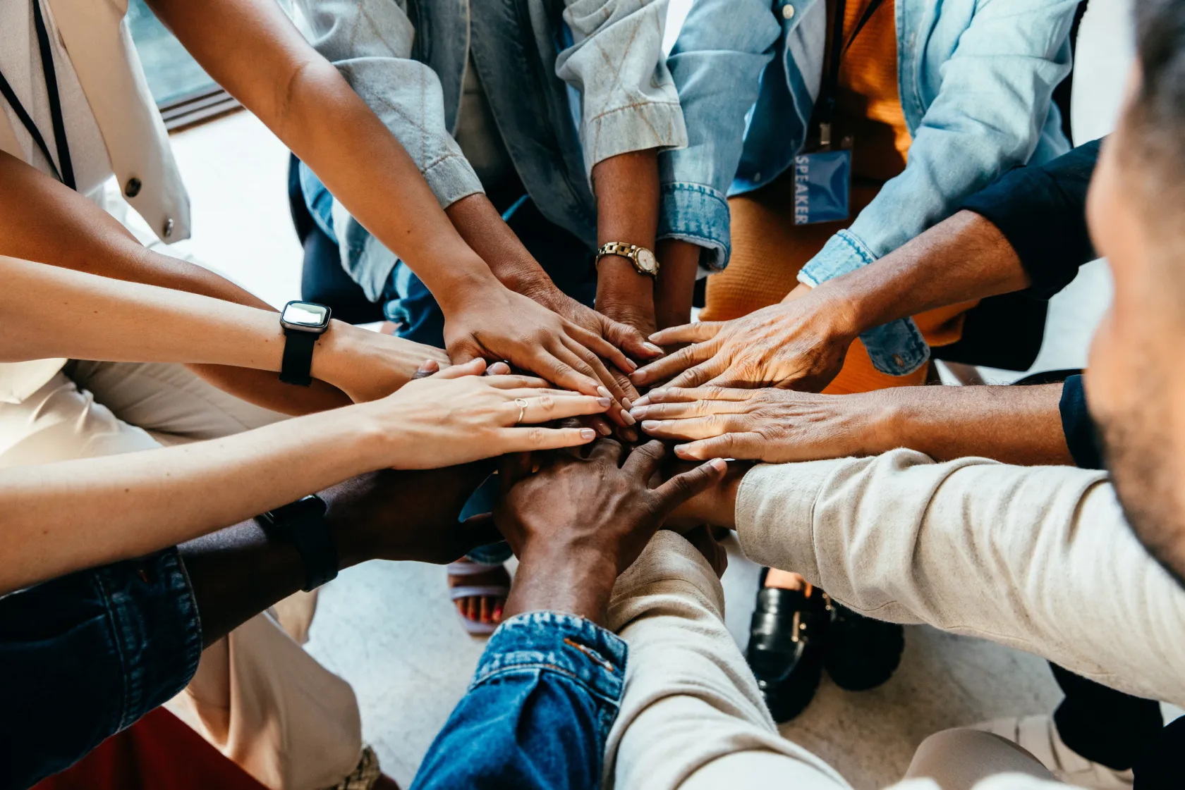 A large team of people circling up and reaching their hands in together