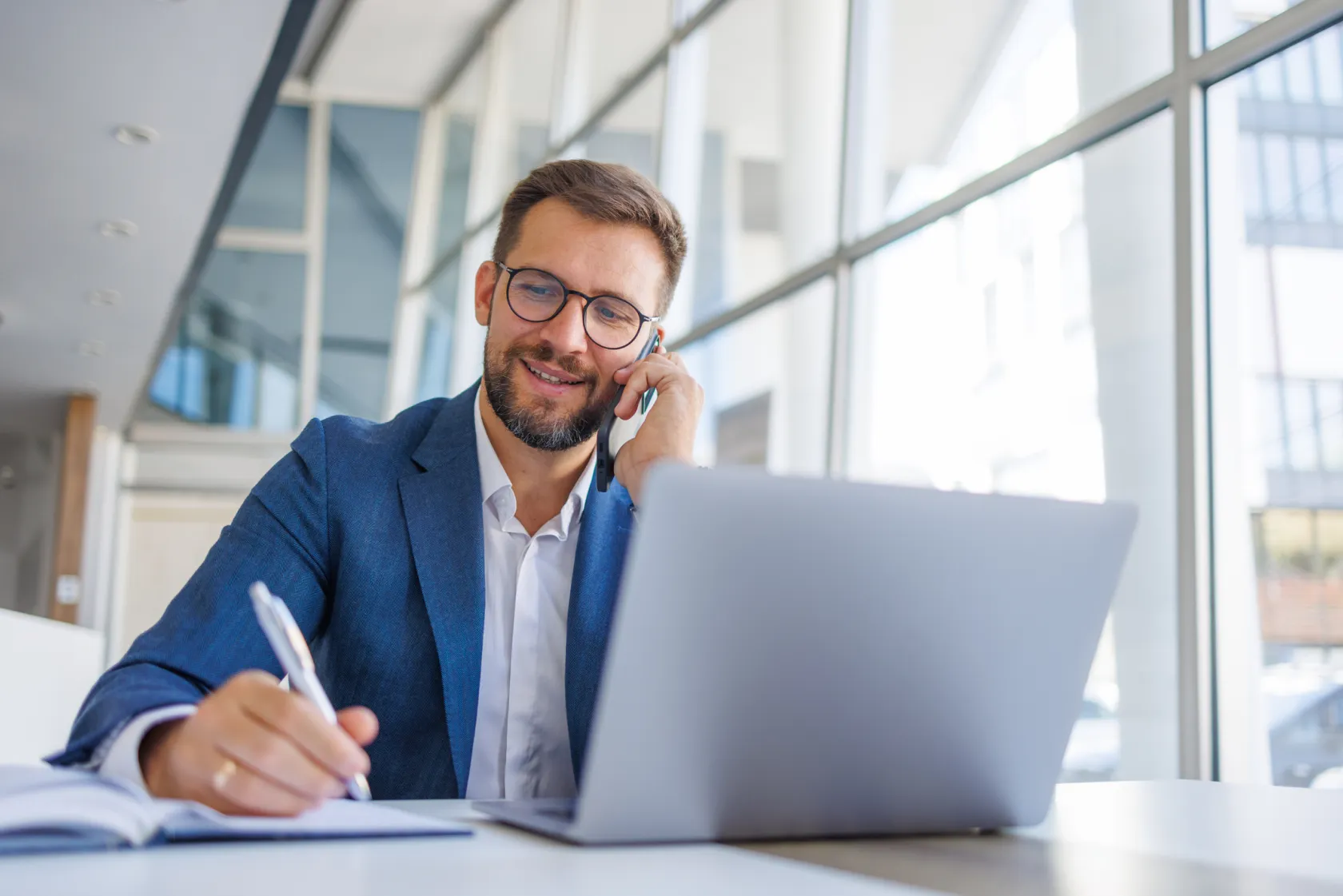 A man writing details down while on the phone at a desk