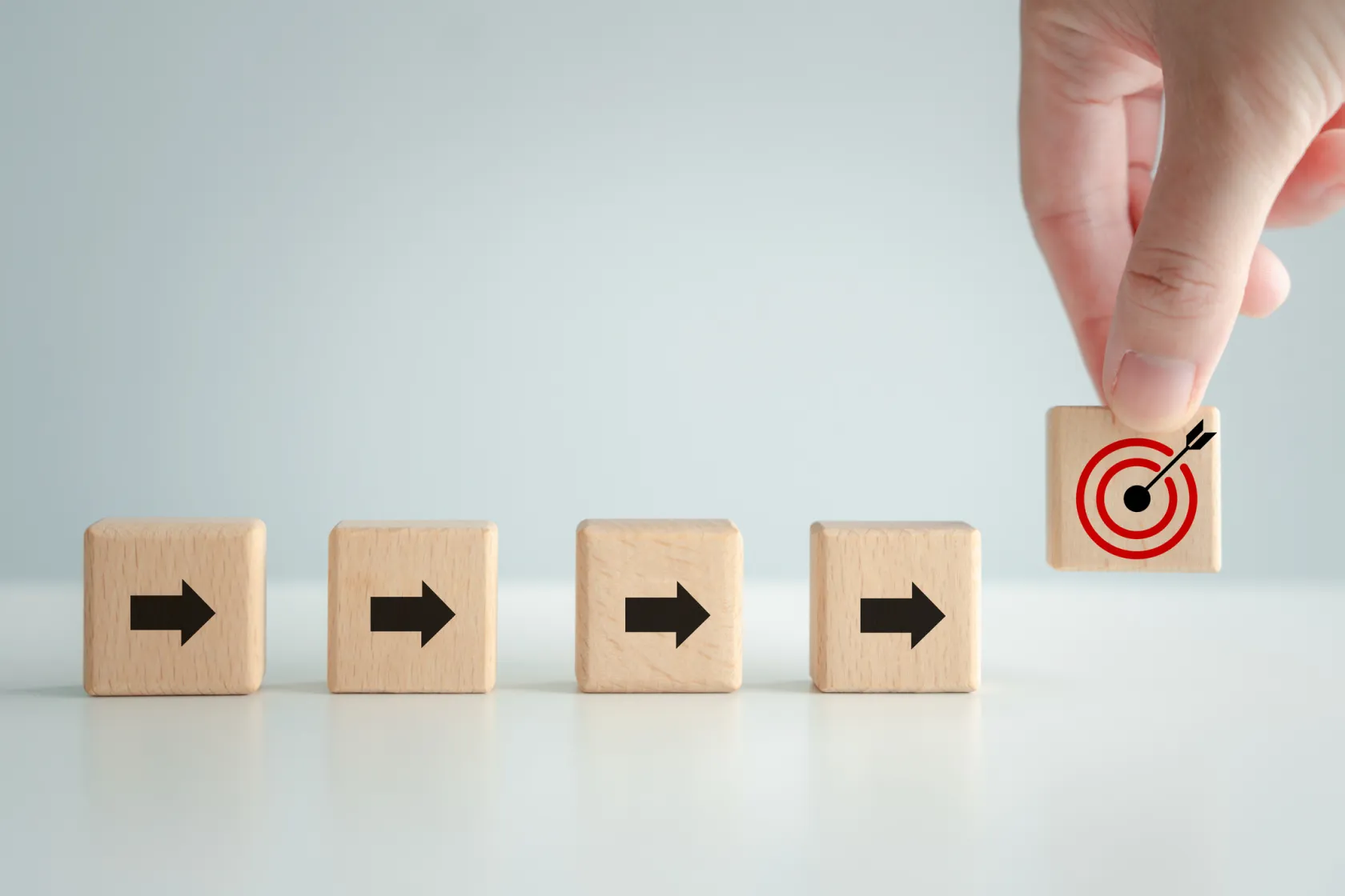 An array of blocks with arrows on them lined up. A hand is picking up another block with a bullseye on it.
