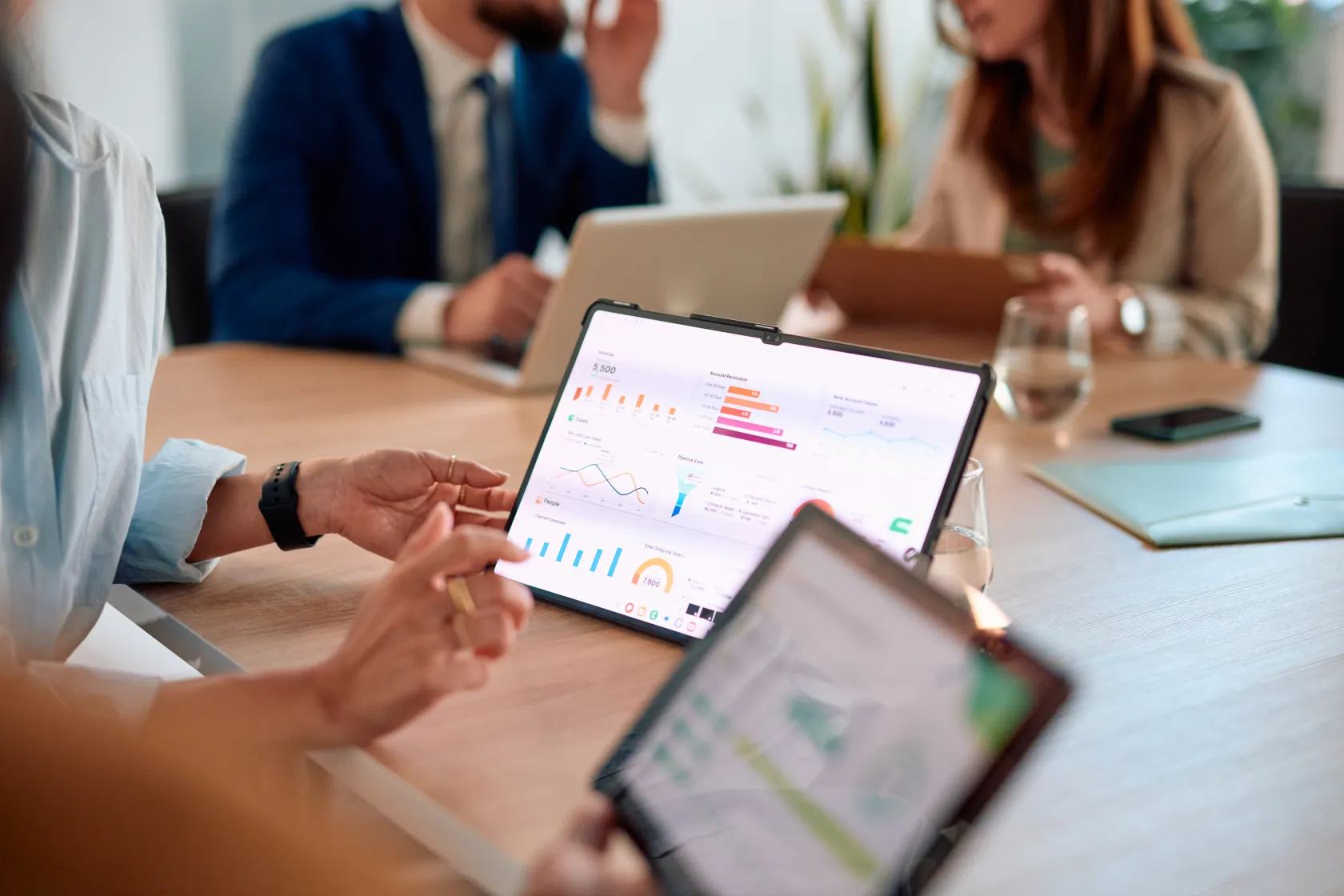 Team member pointing to a business analytics dashboard on a tablet during a meeting with colleagues