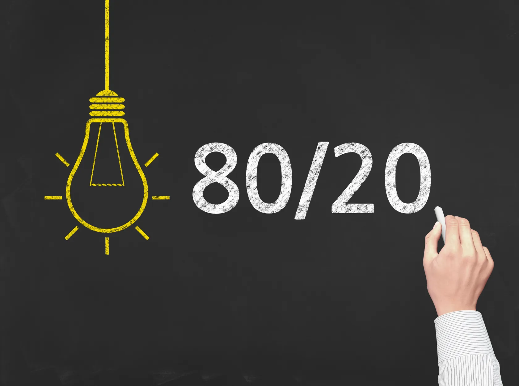 Hand writing "80/20" in chalk on a blackboard next to a drawn light bulb, illustrating the Pareto Principle