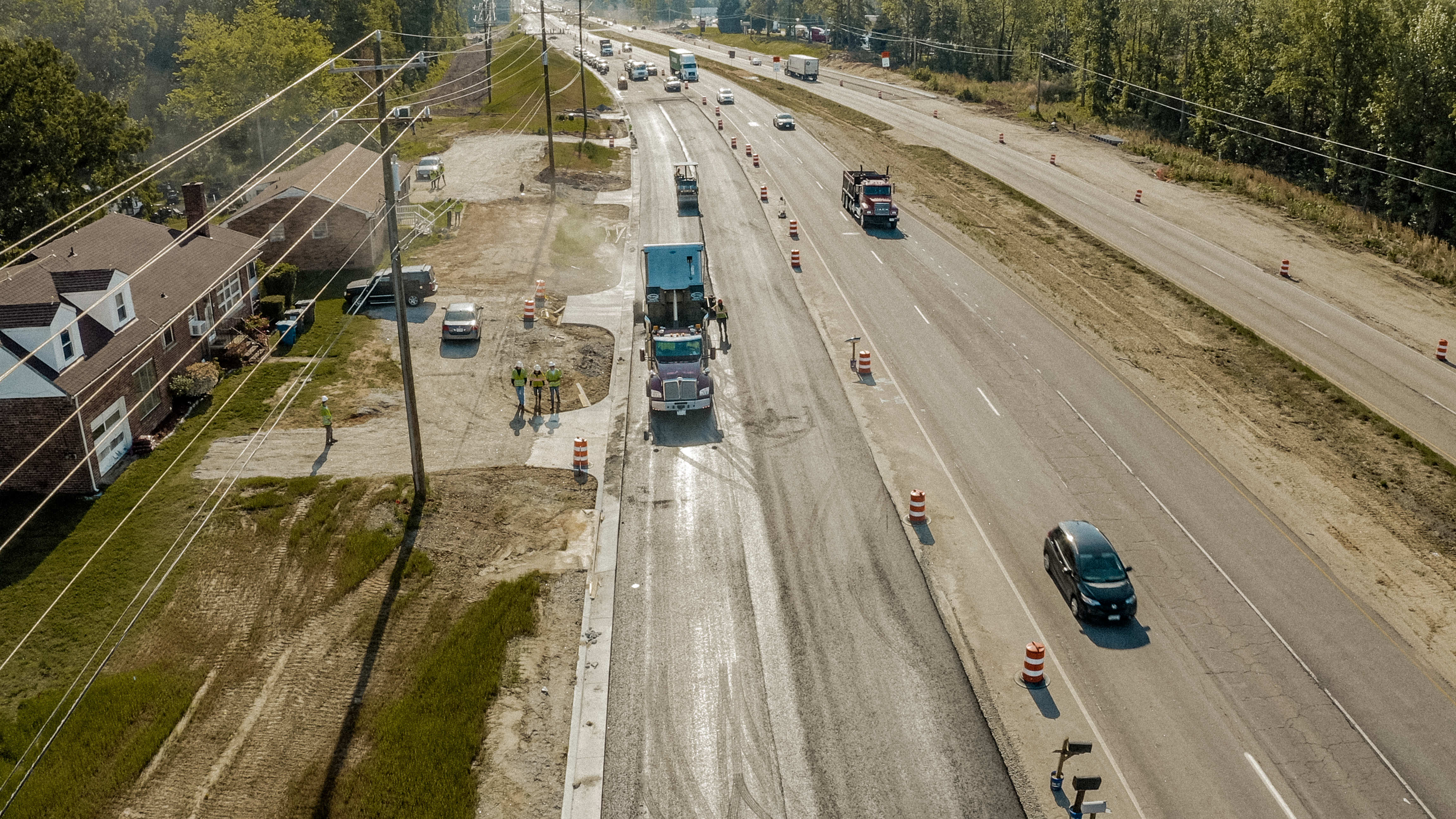 Shirley Gap 64: Aerial view of dump trucks and paving equipment working beside traffic.