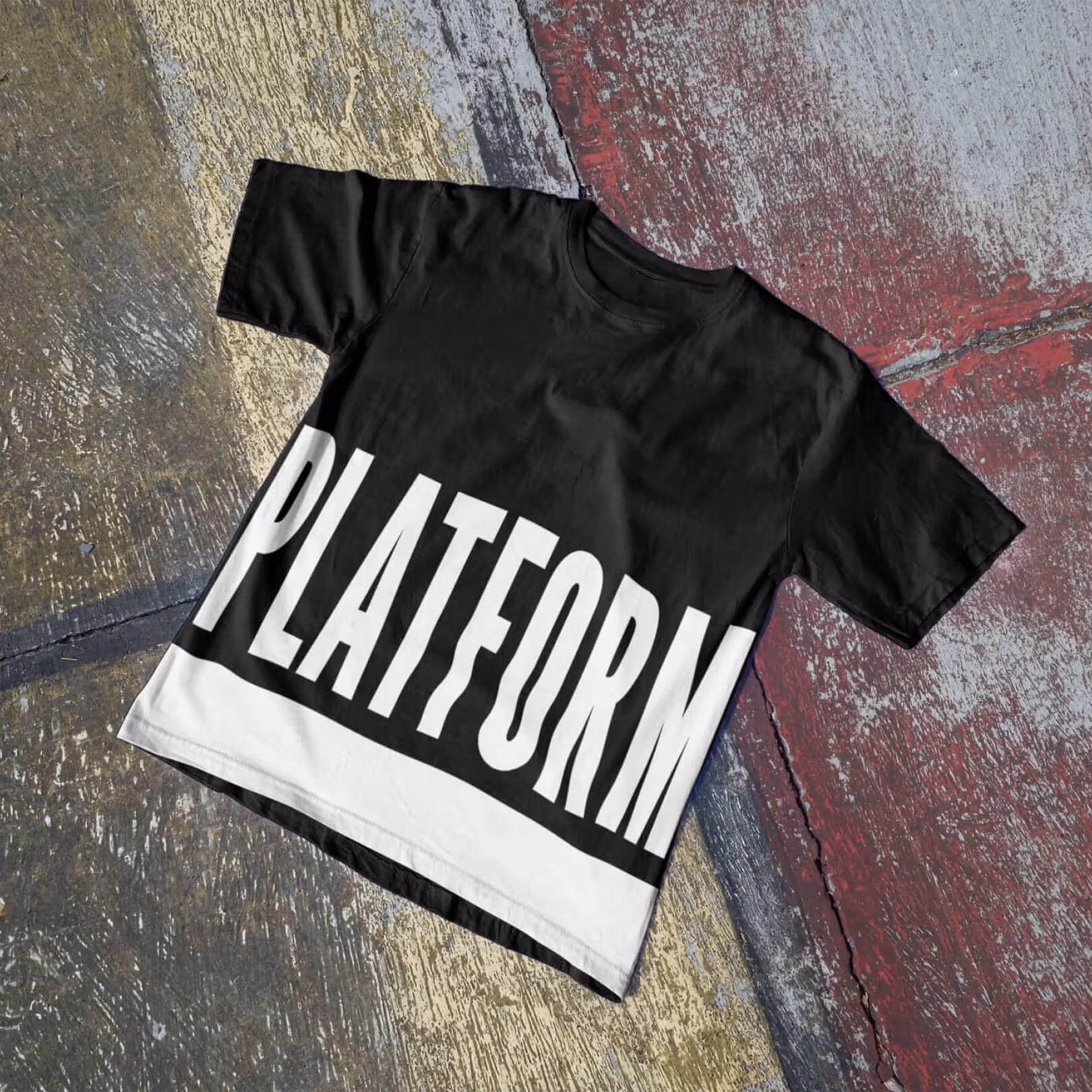 Black t-shirt laid flat on pavement with the Platform Studios logo printed across the front in white.