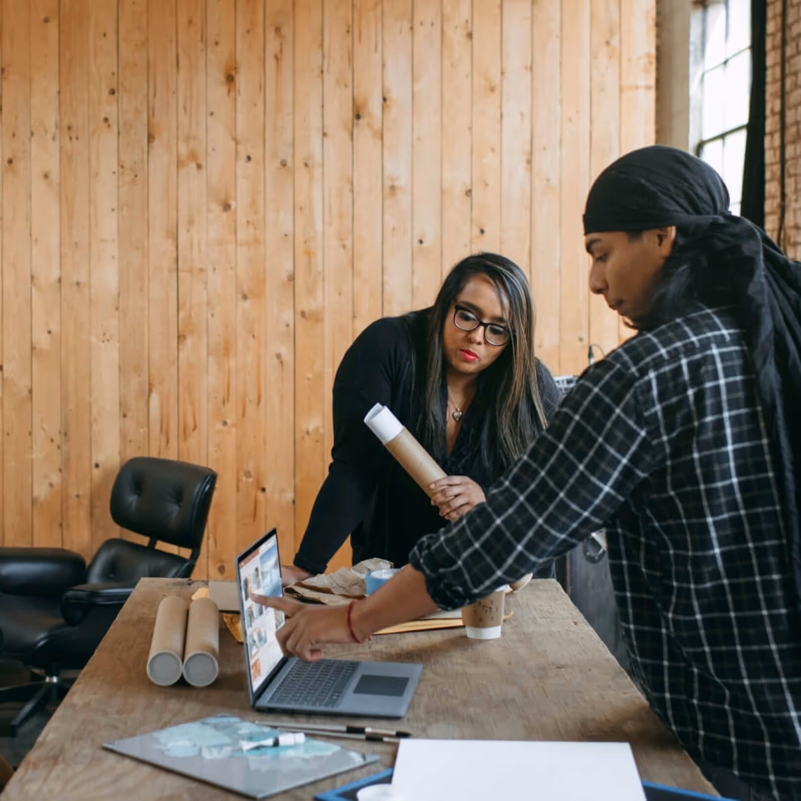 Two people collaborating at a wooden table reviewing printed materials and a laptop during community ecosystem mapping research for Platform Studios.