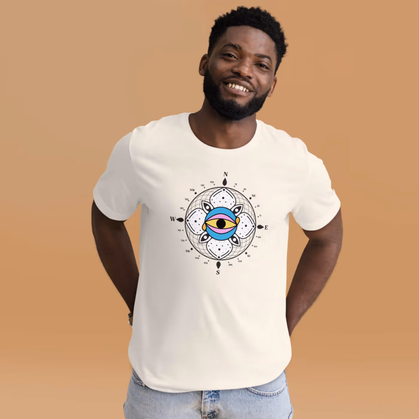 Smiling Black man wearing white t-shirt with The Infinite Search compass logo design featuring colorful eye symbol and directional elements, posed against tan background