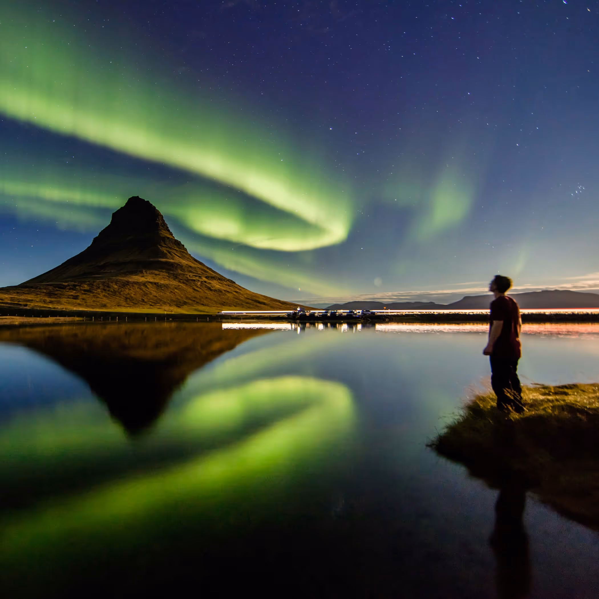 Northern lights dancing over mountain reflected in still water at dusk