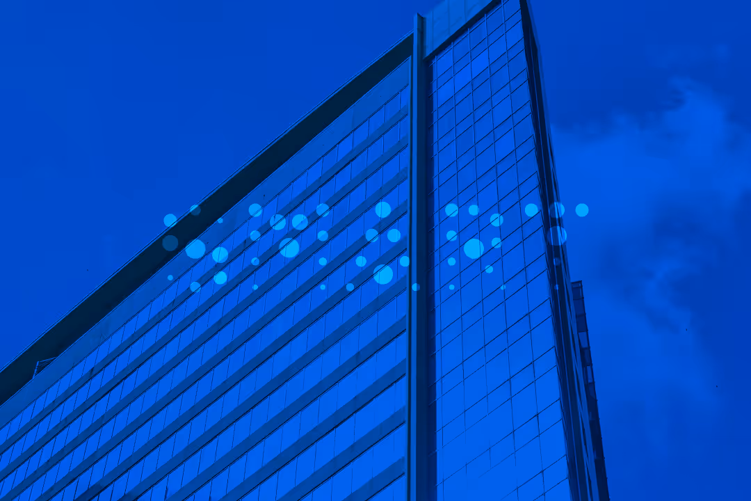 Modern glass office building photographed from below with dramatic blue lighting and geometric patterns against blue sky