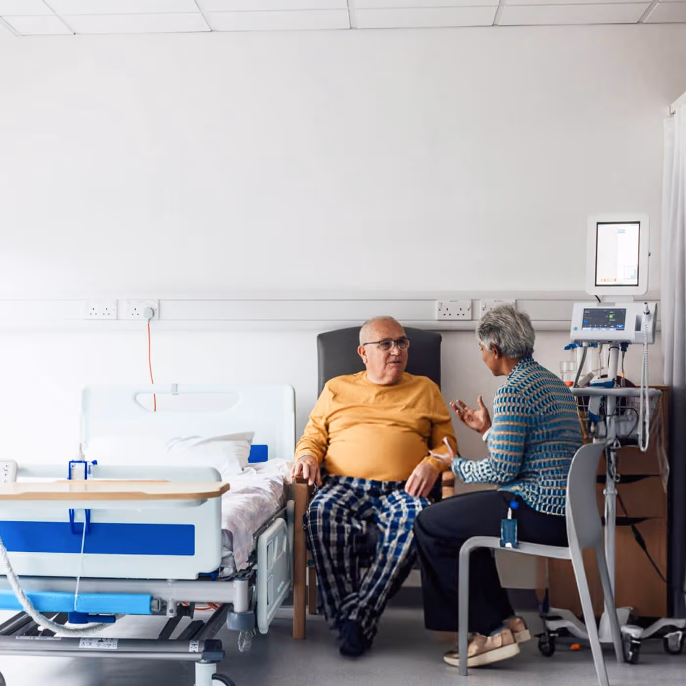 Elderly male patient in hospital bed with female visitor in caring conversation