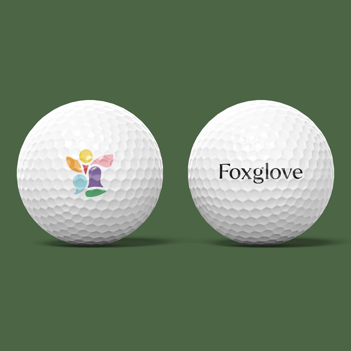 Two white golf balls on a green background, one with a colorful abstract logo and the other with the word 'Foxglove'.
