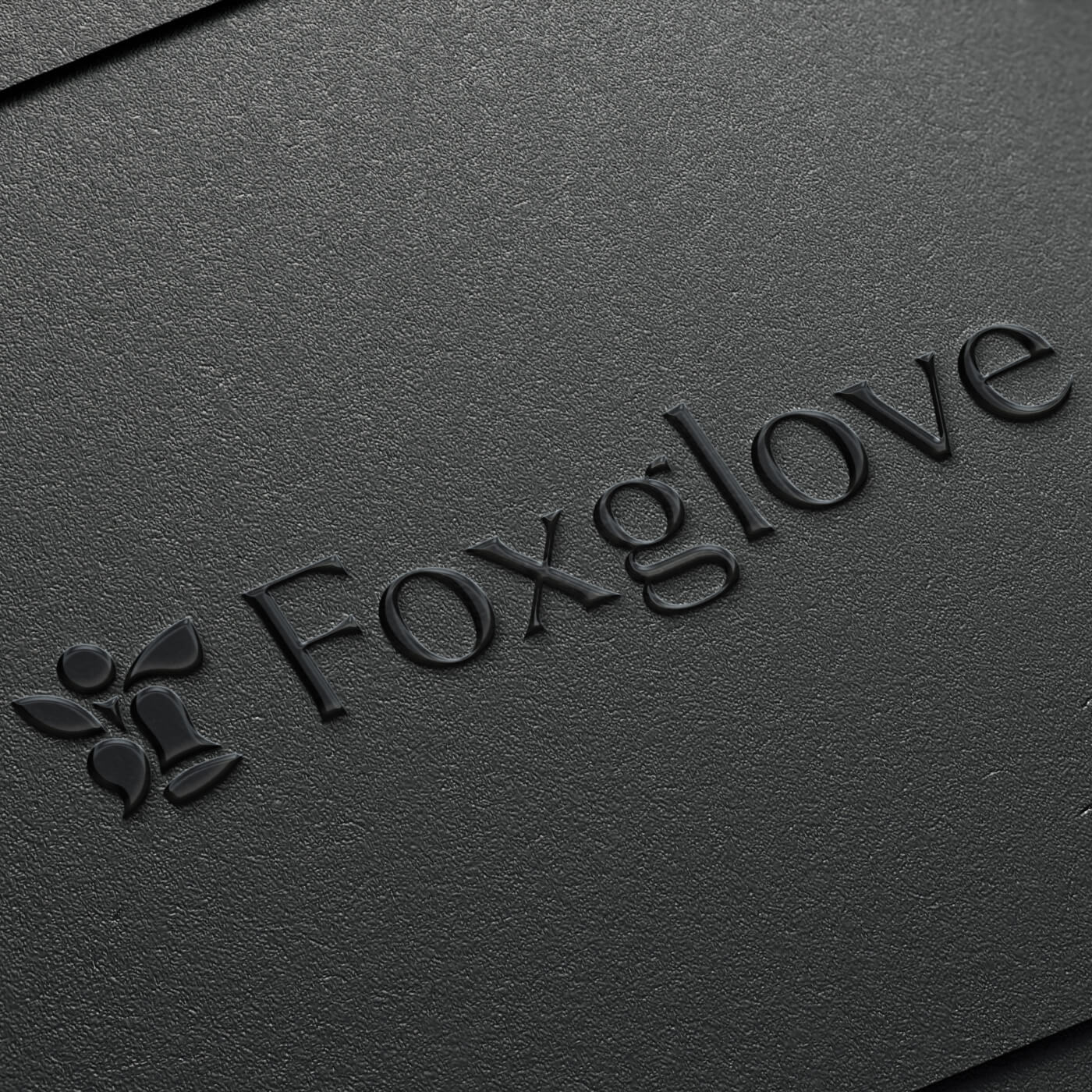 Embossed black logo with stylized butterfly icon and the text 'Foxglove' on textured black paper.