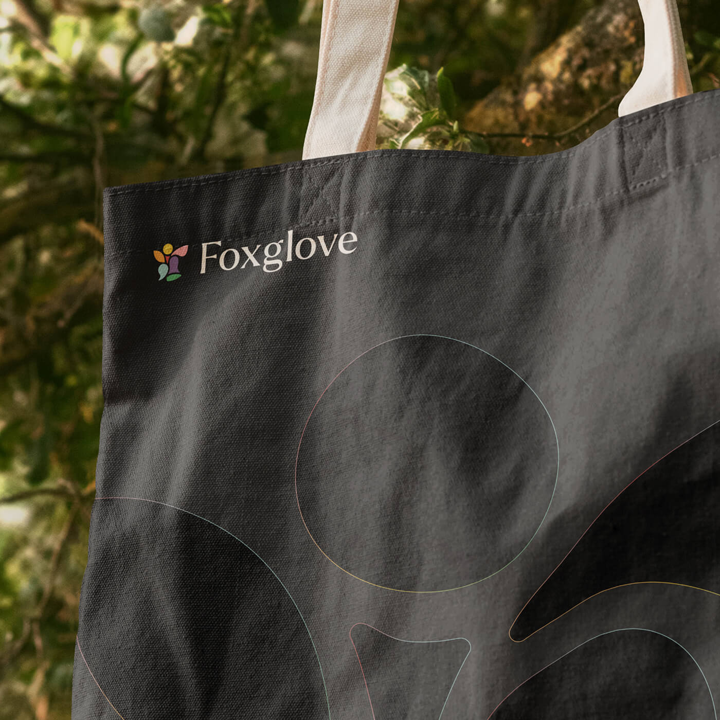 Black tote bag with cream handles featuring the Foxglove logo and brand name in white text.