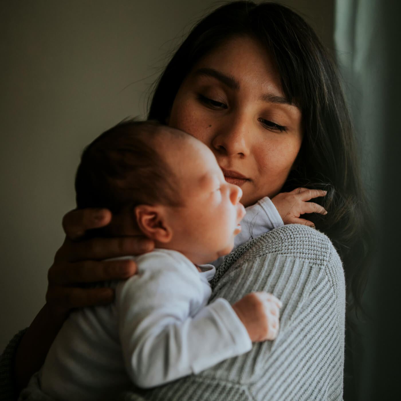 Woman gently cradling a sleeping newborn baby close to her shoulder.