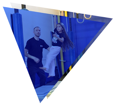 Man assisting a young girl practicing a gymnastic or aerial silk routine indoors.