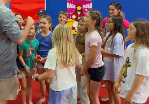 Group of children gathered indoors listening attentively to an adult.