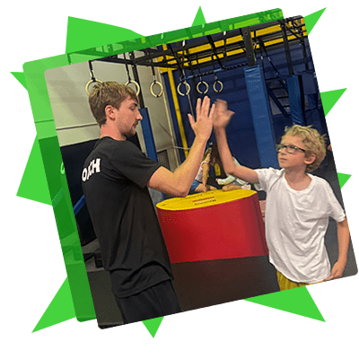 Young adult and child giving a high-five in a gym with rings and climbing equipment.