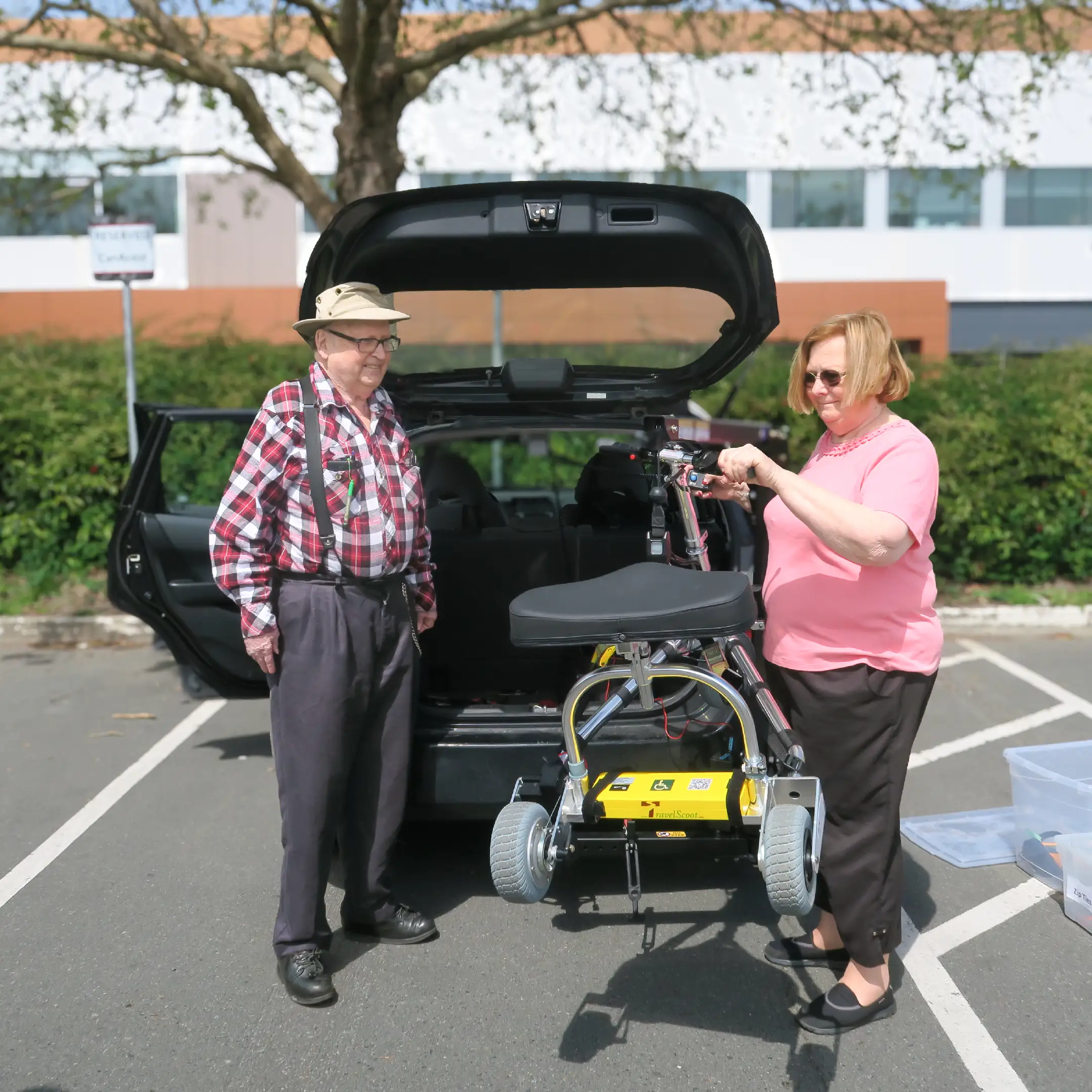 A couple standing at the back of a van with CanAssist's hitch lift lifting a mobility scooter into the trunk
