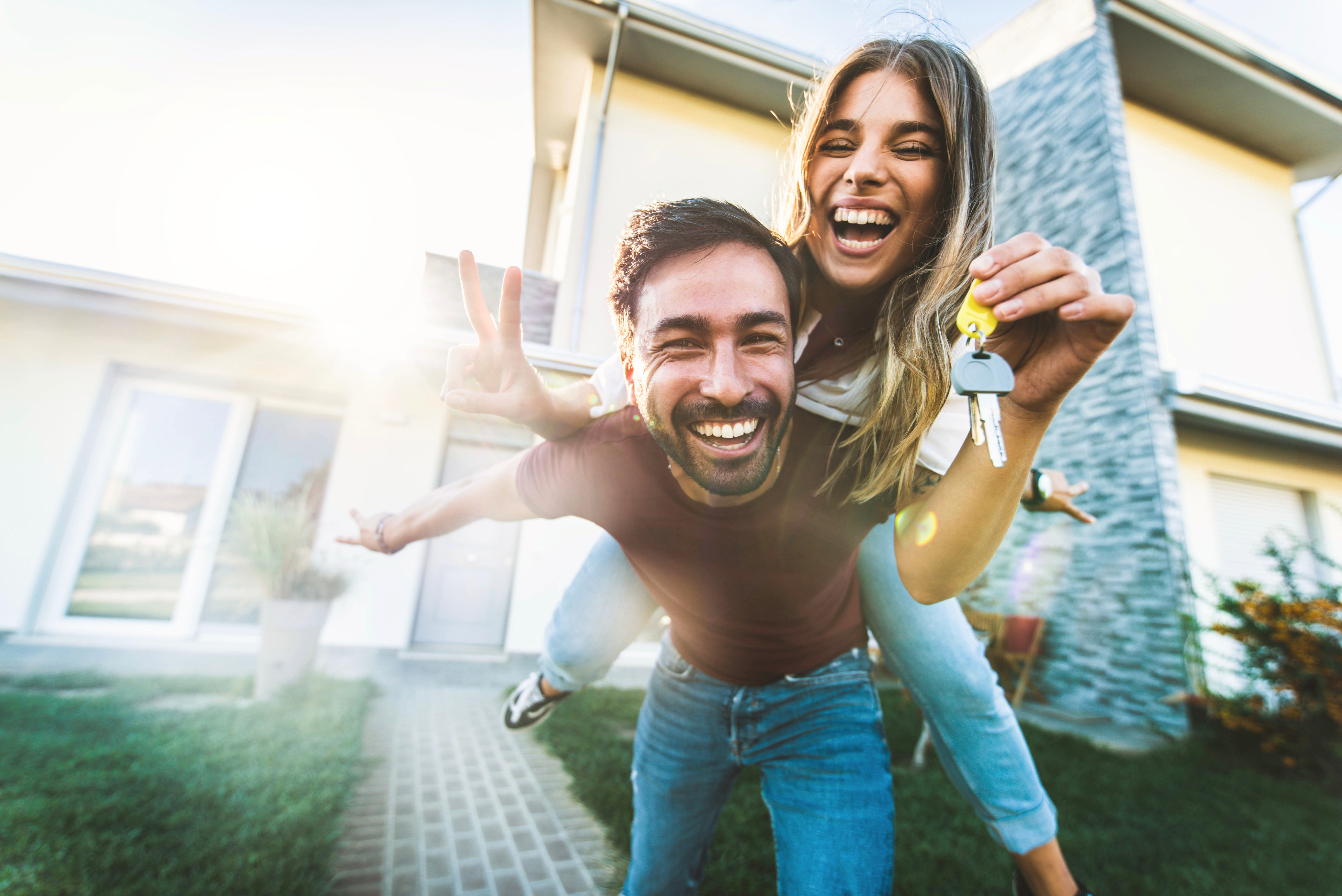 Happy excited couple holding house keys in front of new first home