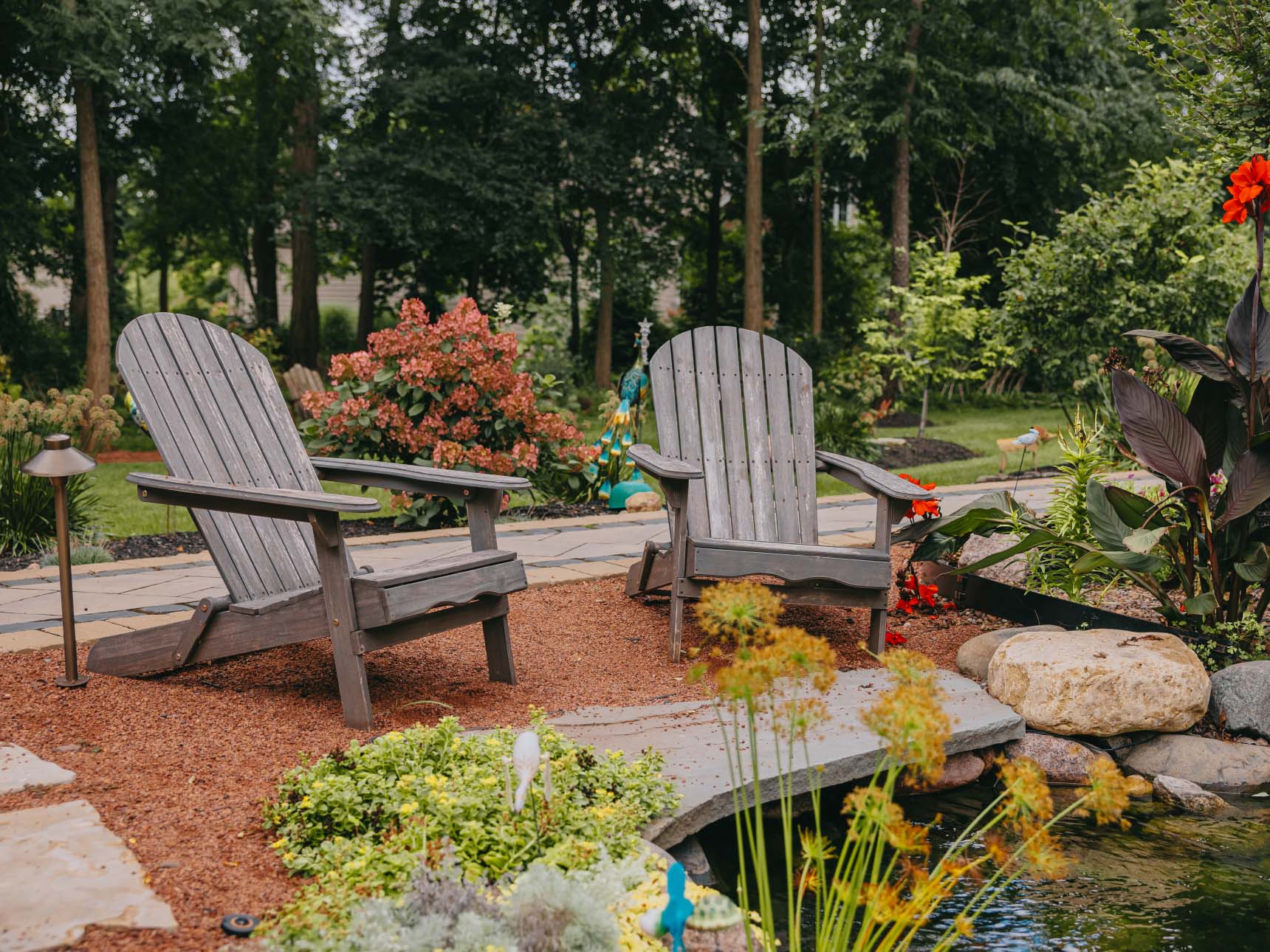 Two wooden Adirondack chairs overlooking peaceful garden pond with lush plants