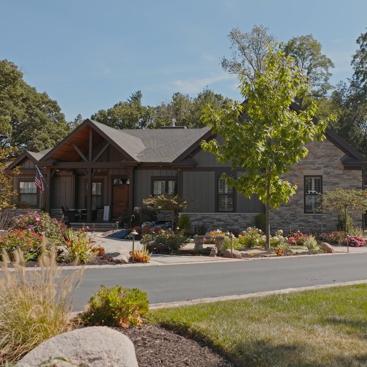 Craftsman-style home with layered landscaping, stone beds and mature plantings by Custom Scapes and Designs