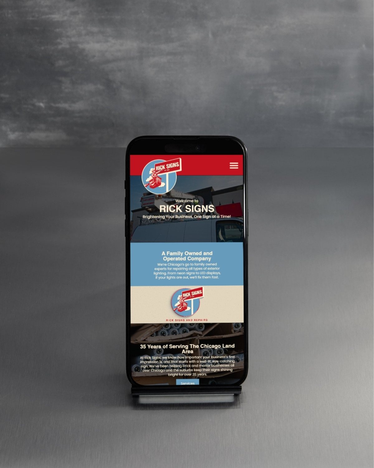 Smartphone on a stand displaying the Rick Signs website homepage.