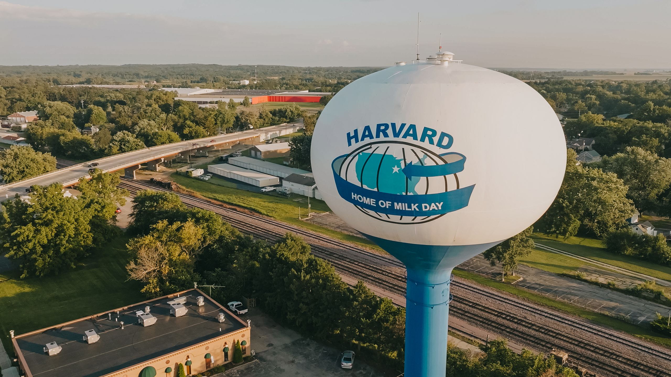 Aerial drone photo of the Harvard, Illinois water tower above town and rail lines at golden hour
