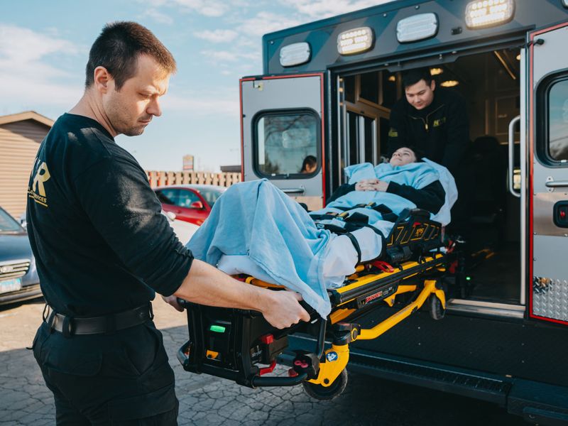 Northwest Rescue paramedic loading a patient on a powered stretcher into the back of an ambulance while a second crew member assists from inside.