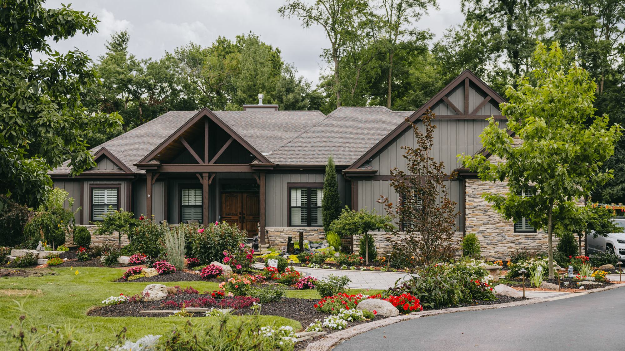 Landscaped front yard with colorful garden beds and a stone walkway by Custom Scapes & Designs