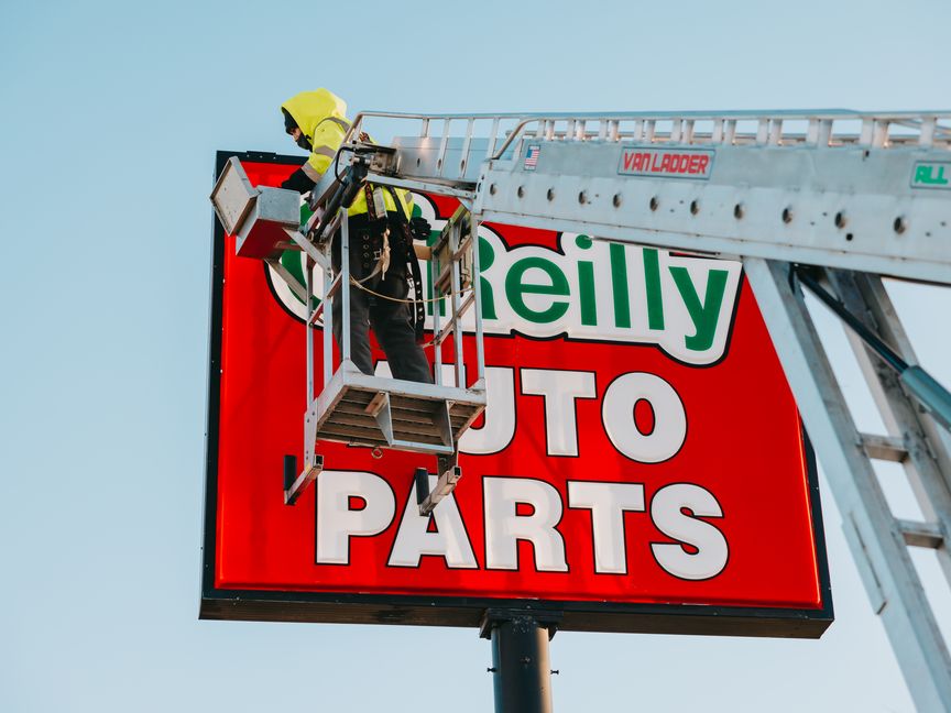 Rick Signs & Repairs technician servicing an O'Reilly Auto Parts pylon sign from an aerial ladder