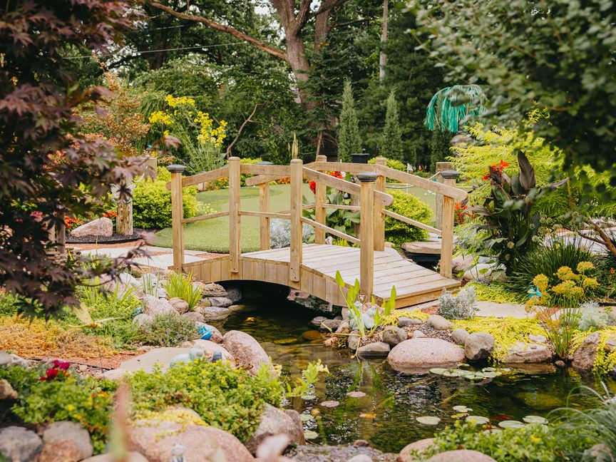 Wooden footbridge over a landscaped koi pond by Custom Scapes & Designs