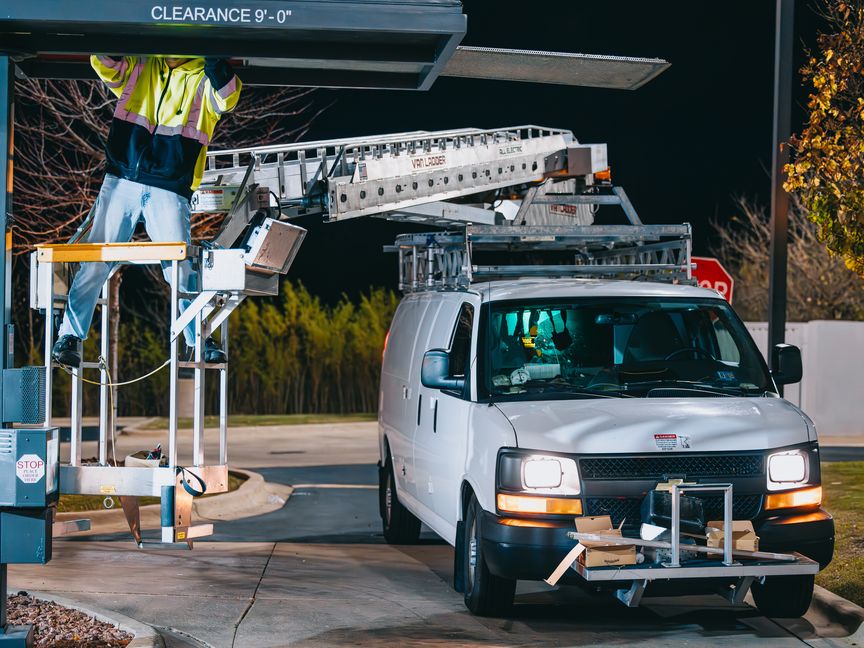 Rick Signs & Repairs service van and ladder on a night repair call under a drive-thru canopy