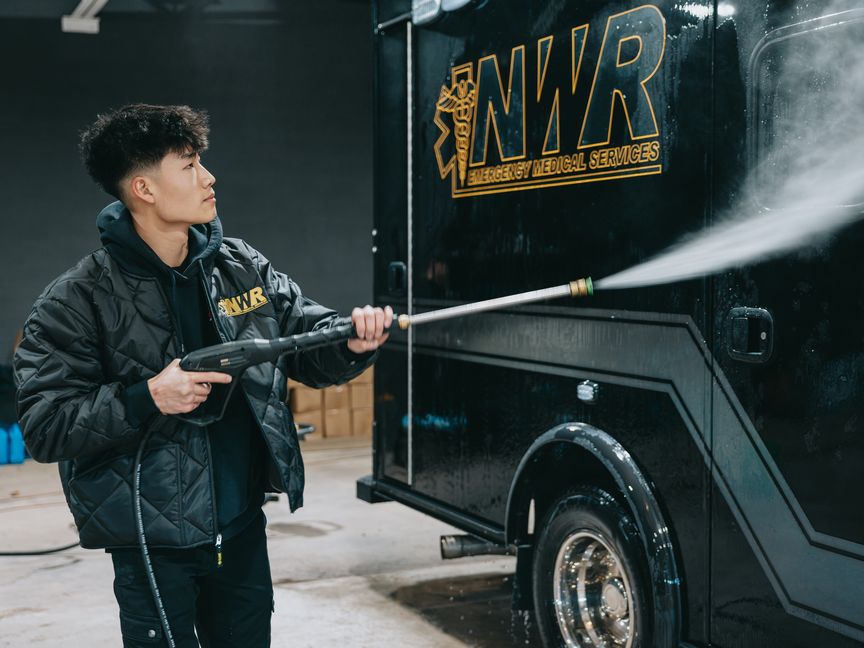 Northwest Rescue crew member pressure washing a black NWR ambulance