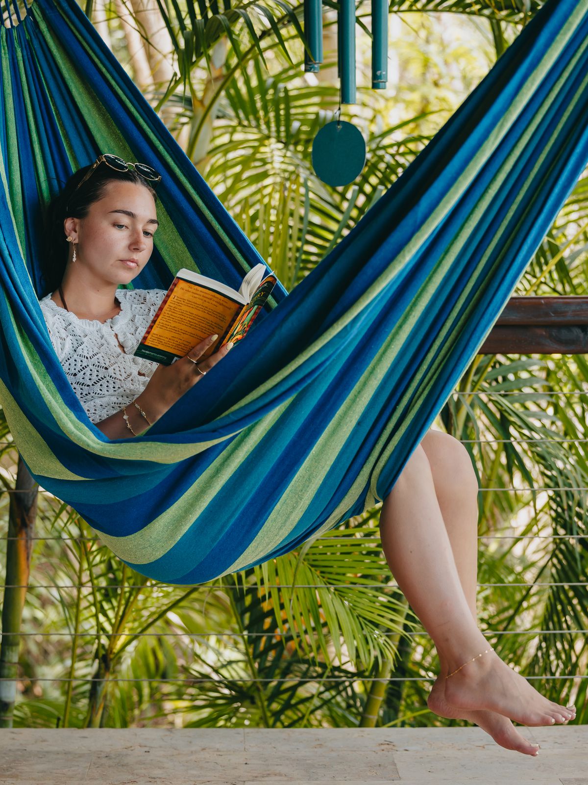 Guest reading a book in a striped hammock surrounded by tropical plants at Moon Cottage
