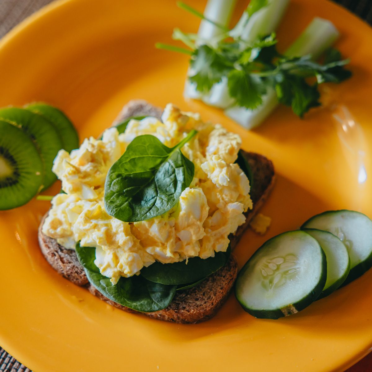 Breakfast of eggs, greens and fruit served on a yellow plate at Moon Cottage