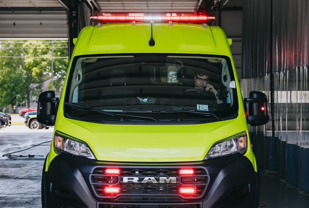 Lime green Stark County Ambulance with red emergency lights on, parked in the station bay