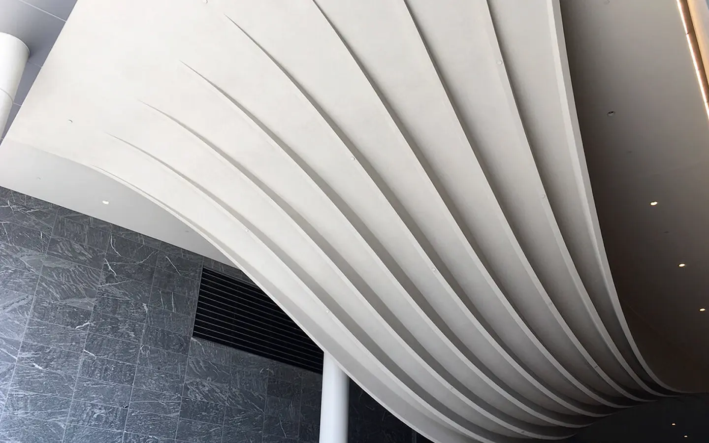 White freeform curved ceiling with ribs above a dark gray marble wall and a white cylindrical column.