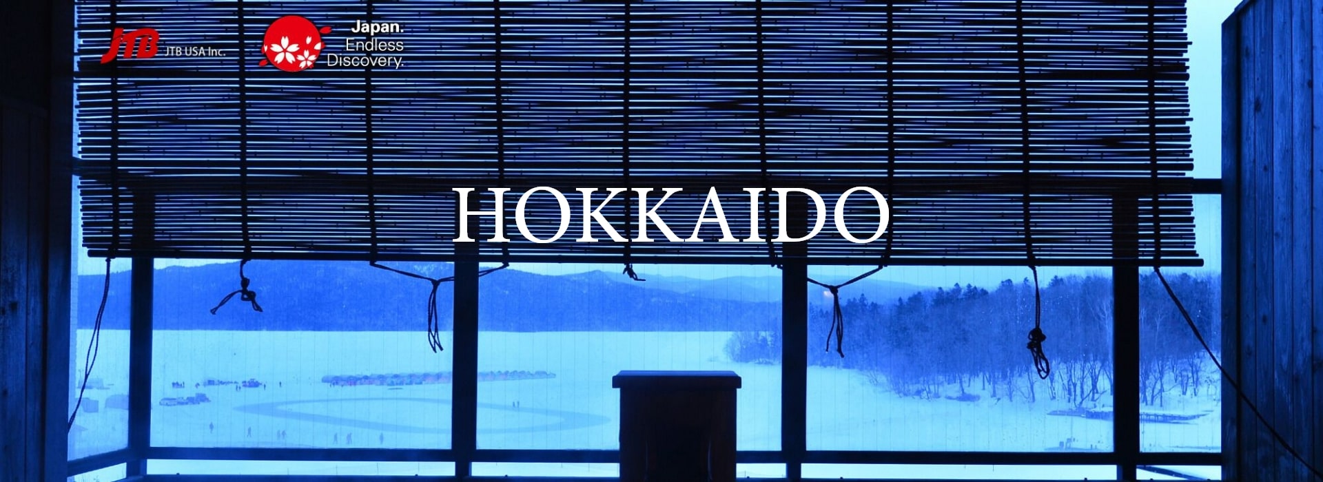 Snow-covered landscape of Hokkaido viewed through traditional bamboo blinds from a warm indoor onsen.