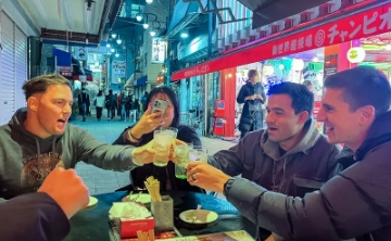 Group of friends enjoying drinks together at an outdoor izakaya in Japan at night