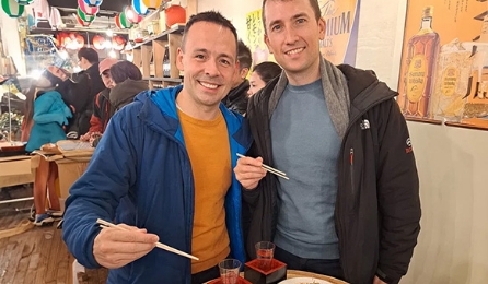 Two friends enjoying Japanese food and sake at a lively local izakaya