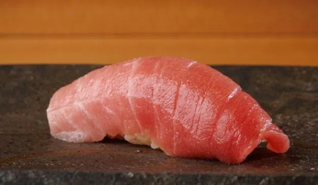 Close-up of a beautifully crafted piece of tuna sushi on a stone plate.